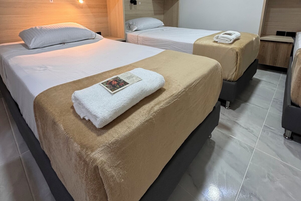 A hotel room with two beds, wooden headboards, and a tiled floor.