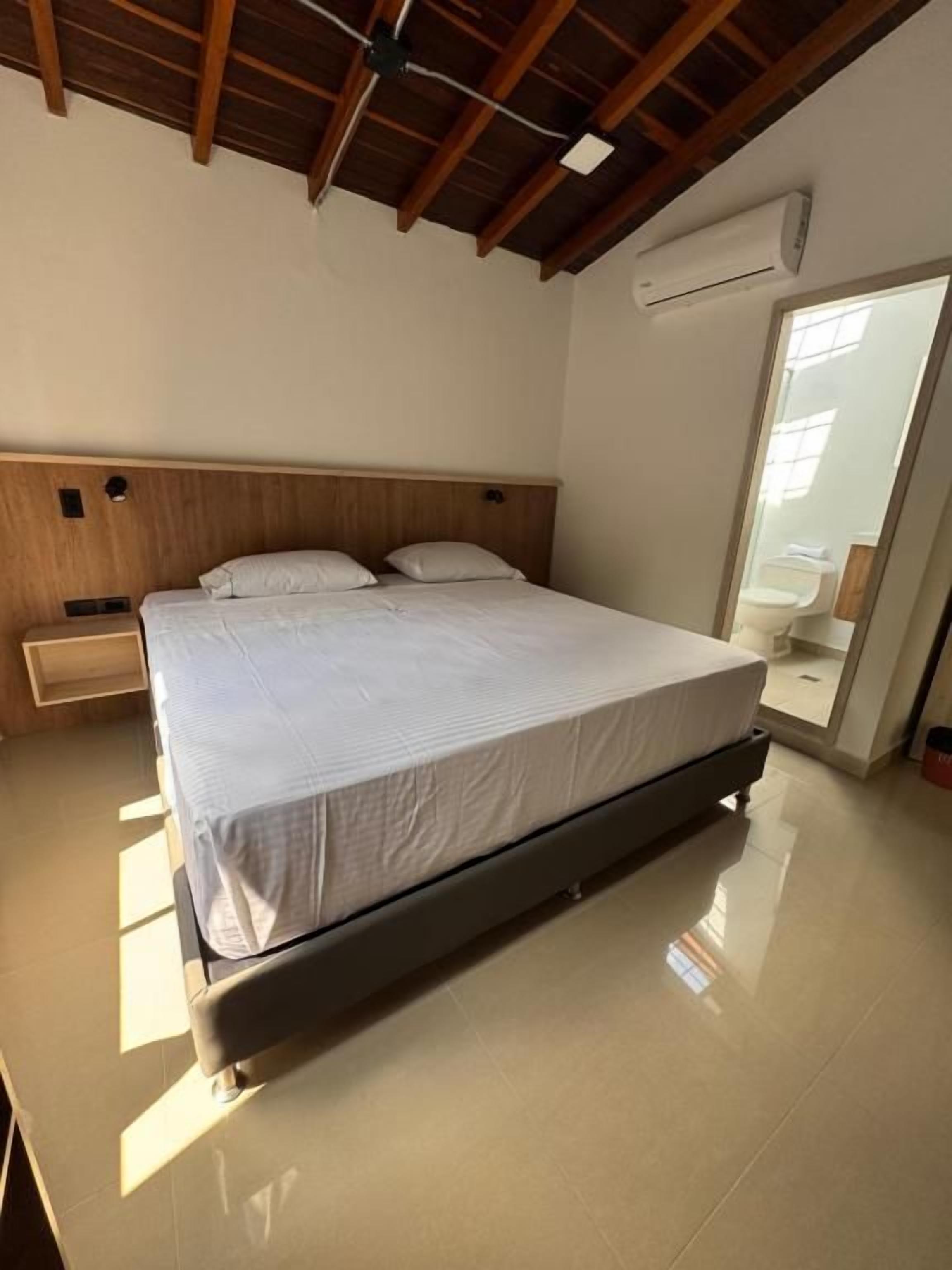 A bedroom with a bed, a nightstand, a wall-mounted air conditioning unit, and a window.