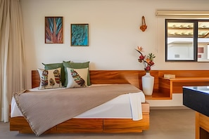A bedroom with a wooden bed, green and patterned pillows, a bedside table, a vase with flowers, and two wall art pieces.