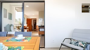 A modern room with a wooden dining table, a sofa, and a kitchen area visible through an open door. - Arara House (Jijoca de Jericoacoara)