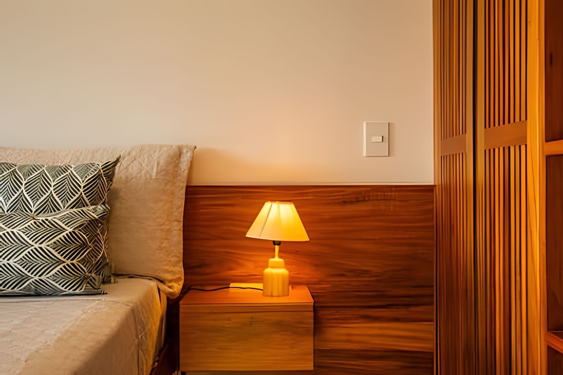 A neatly made bed with patterned pillows, a bedside lamp, and a wooden headboard.