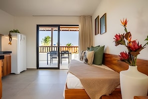 A bedroom with a bed, a desk, a chair, a balcony, and a view of the outdoors.