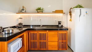 A compact kitchen with a black countertop, wooden cabinets, a white refrigerator, and a coffee machine. - Arara House (Jijoca de Jericoacoara)