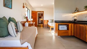 A modern hotel room with a bed, bedside table, lamp, and a view of the kitchen area. - Arara House (Jijoca de Jericoacoara)