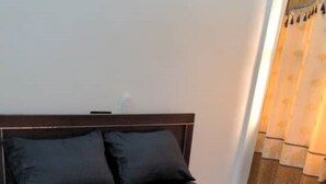 A bed with a dark headboard and two pillows, a small rug, and a curtain partially visible.