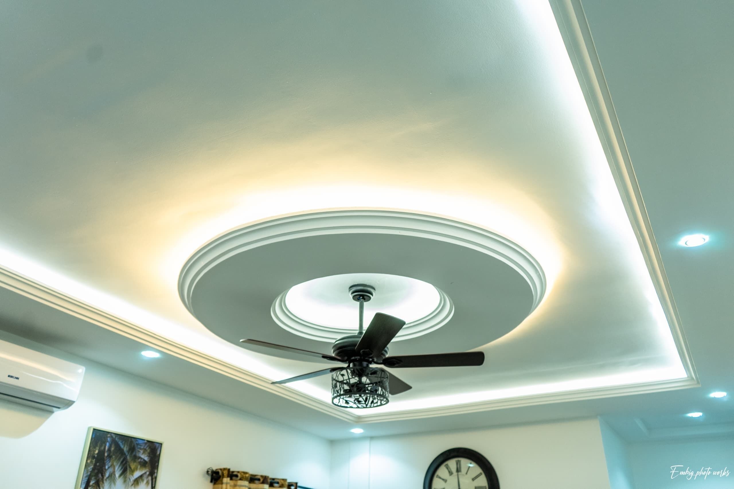 Een plafond met een centrale ronde lamp en een plafondventilator.
