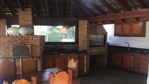 Cuina rústica amb un forn de rajol, armaris de fusta i zona de menjador amb taula i caires.