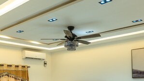 A modern living room with a ceiling fan, recessed lighting, a flat-screen TV, leather sofas, a glass coffee table, and a TV stand.