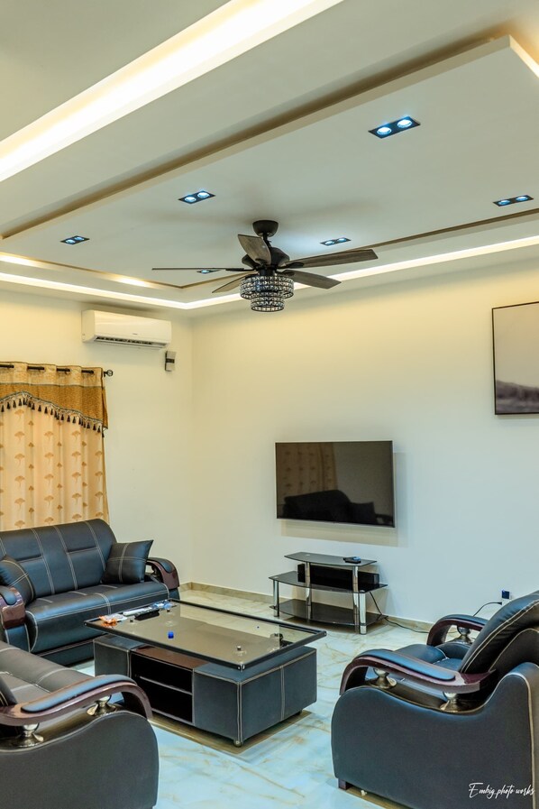 Un salon moderne doté d’un ventilateur de plafond, d’un éclairage encastré, d’un téléviseur à écran plat, de canapés en cuir, d’une table basse en verre et d’un meuble pour téléviseur.