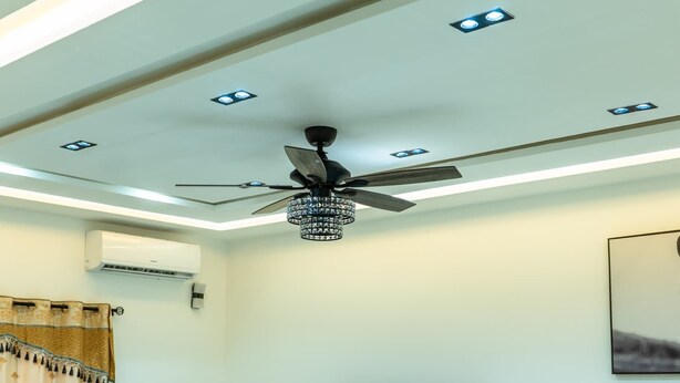 A living room with a ceiling fan, recessed lighting, a flat-screen TV, a sofa, a coffee table, and a massage chair.
