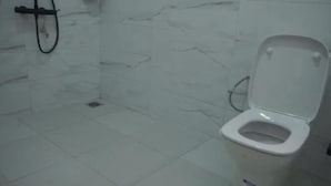 A bathroom with a white toilet, a shower area, and a tiled floor.