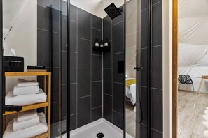 Shower area features a handheld showerhead and a shelf for towels.