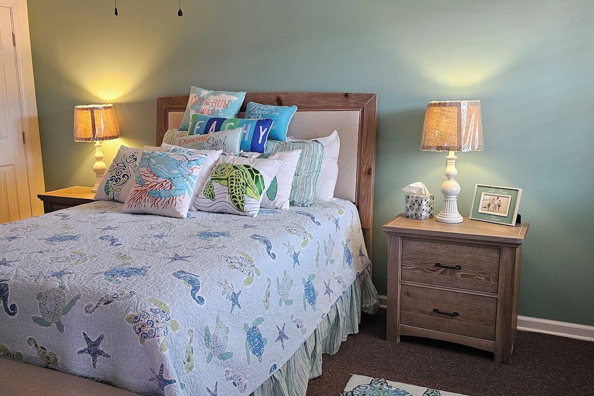 A bedroom with a bed, two nightstands, a wooden door, and a wall with a picture frame.