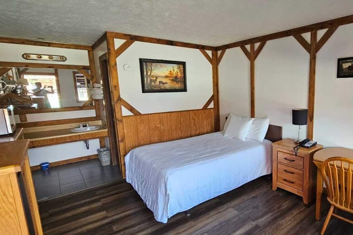 A bedroom with a wooden headboard, a bed, a desk with a chair, a nightstand, and a mirror.