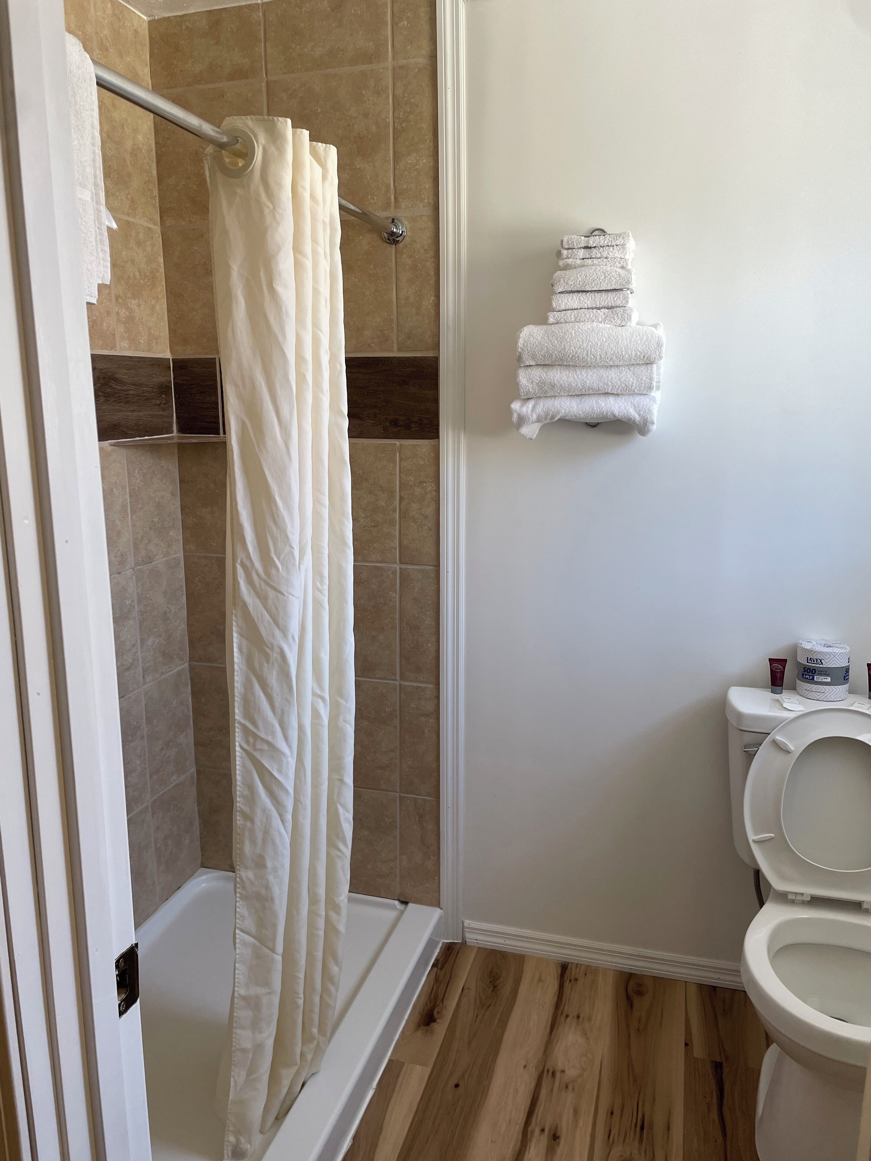 Un baño con ducha, inodoro y una pila de toallas en la pared.