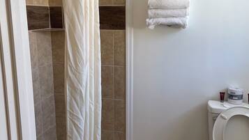 Un baño con ducha, inodoro y una pila de toallas en la pared.