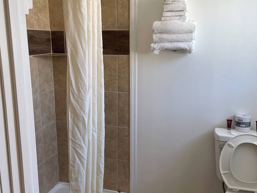 Un baño con ducha, inodoro y una pila de toallas en la pared.