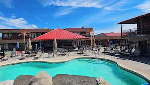A swimming pool with lounge chairs and umbrellas, surrounded by a fenced area with a building in the background. - Beverly hills inn (Aberdeen)