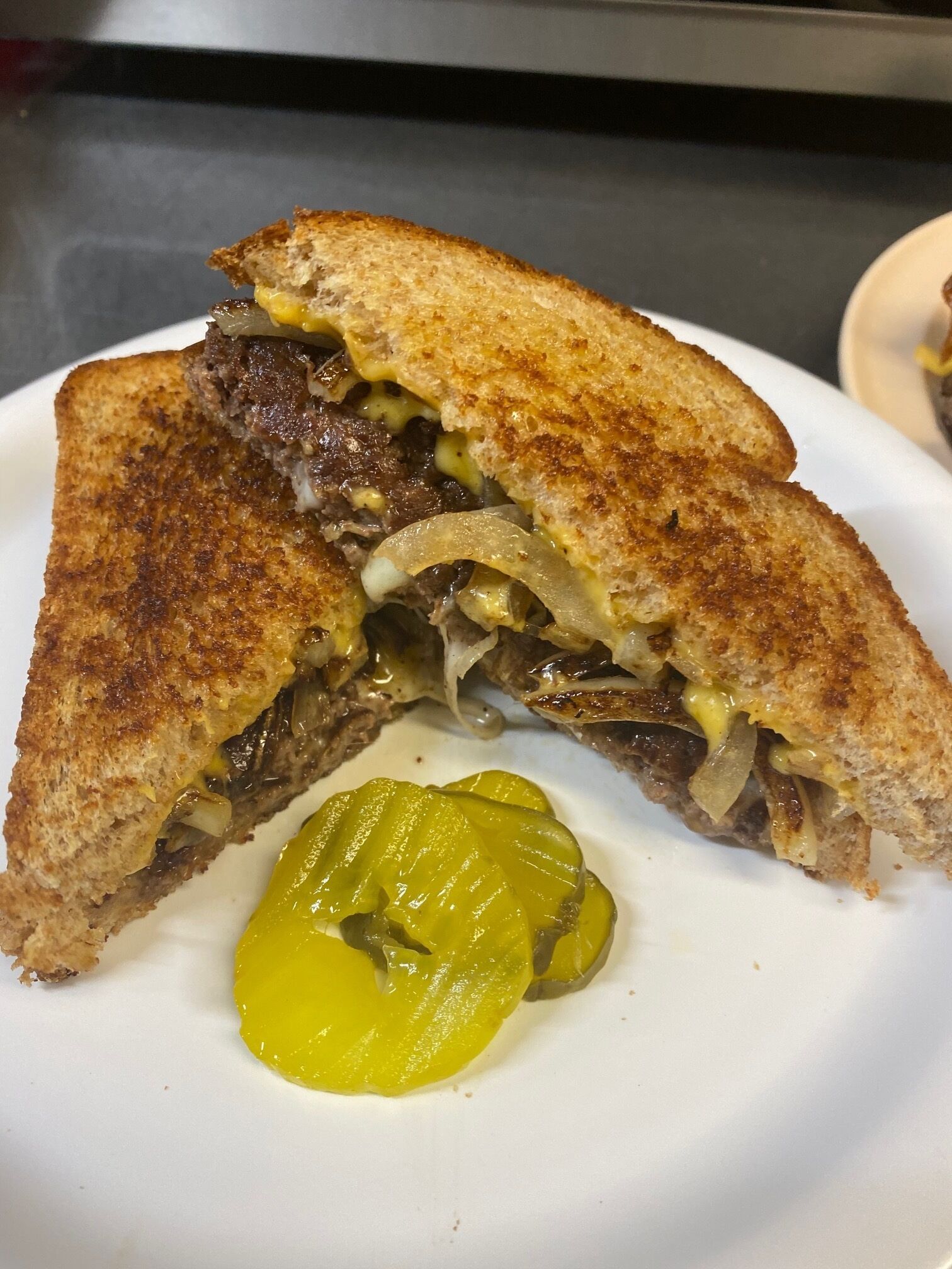 A grilled sandwich with pickles on a white plate.