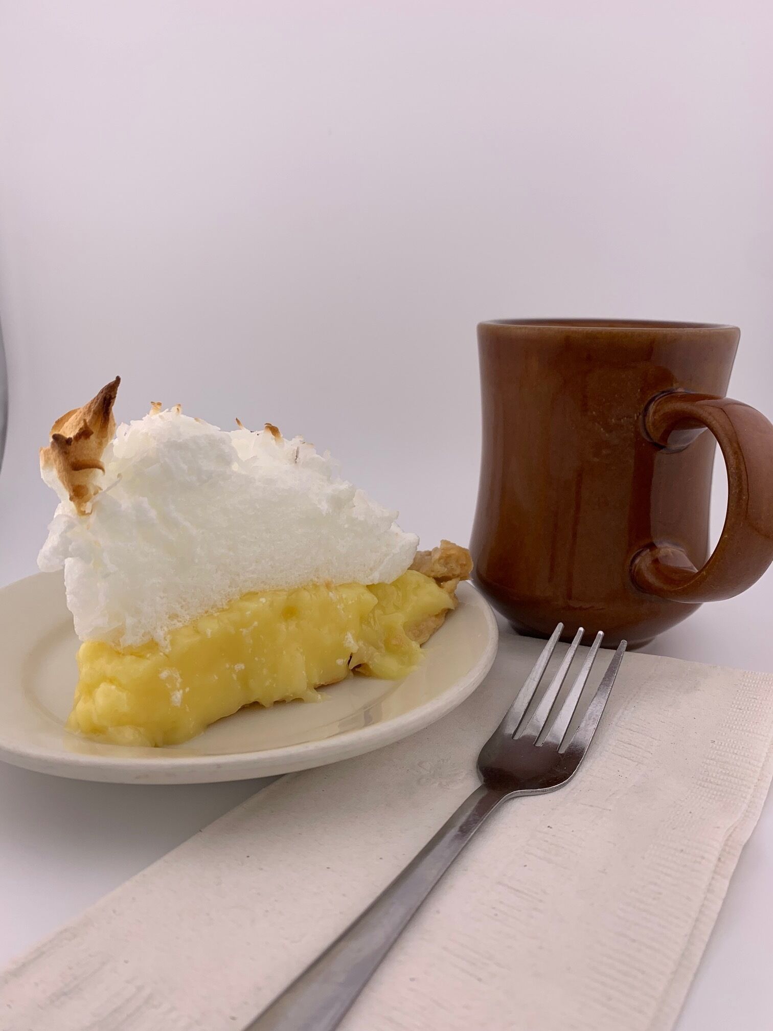Una fetta di torta con una crosta friabile e un ripieno cremoso, servita su un piatto bianco accanto a una tazza marrone.