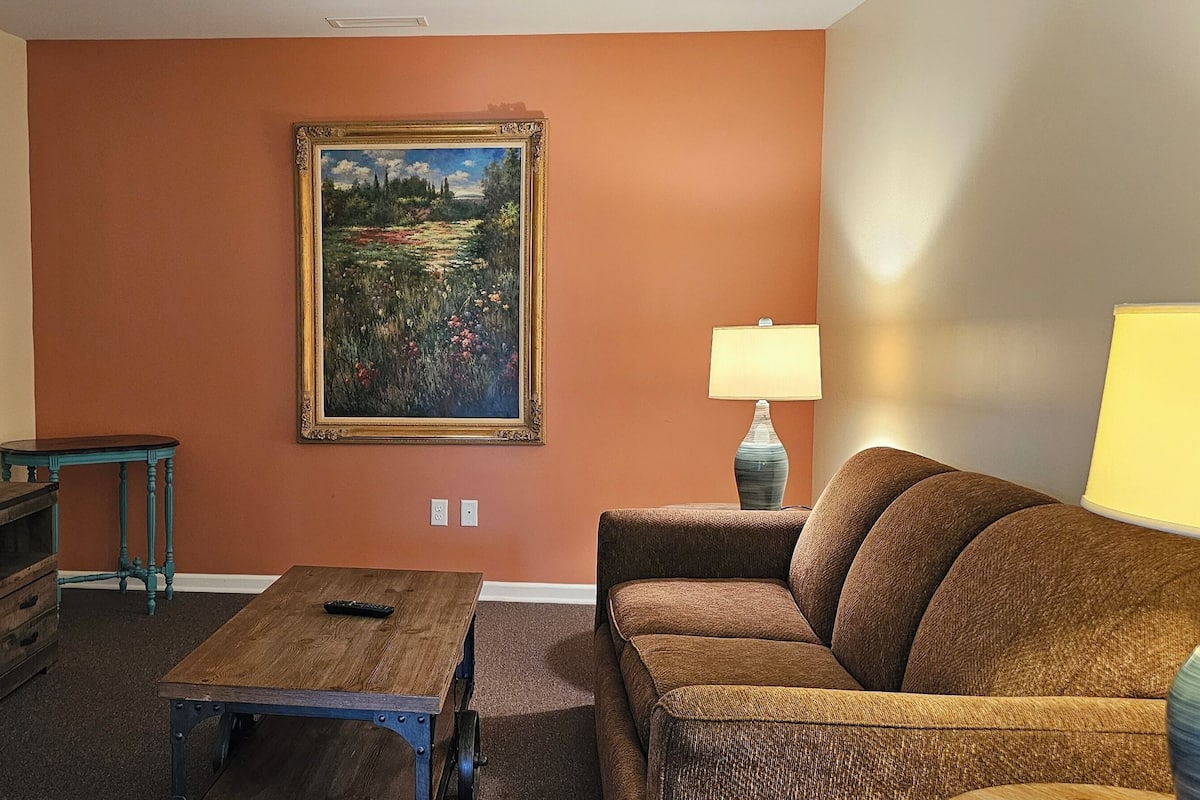 A living room with a television, a painting, a sofa, a coffee table, and a lamp.