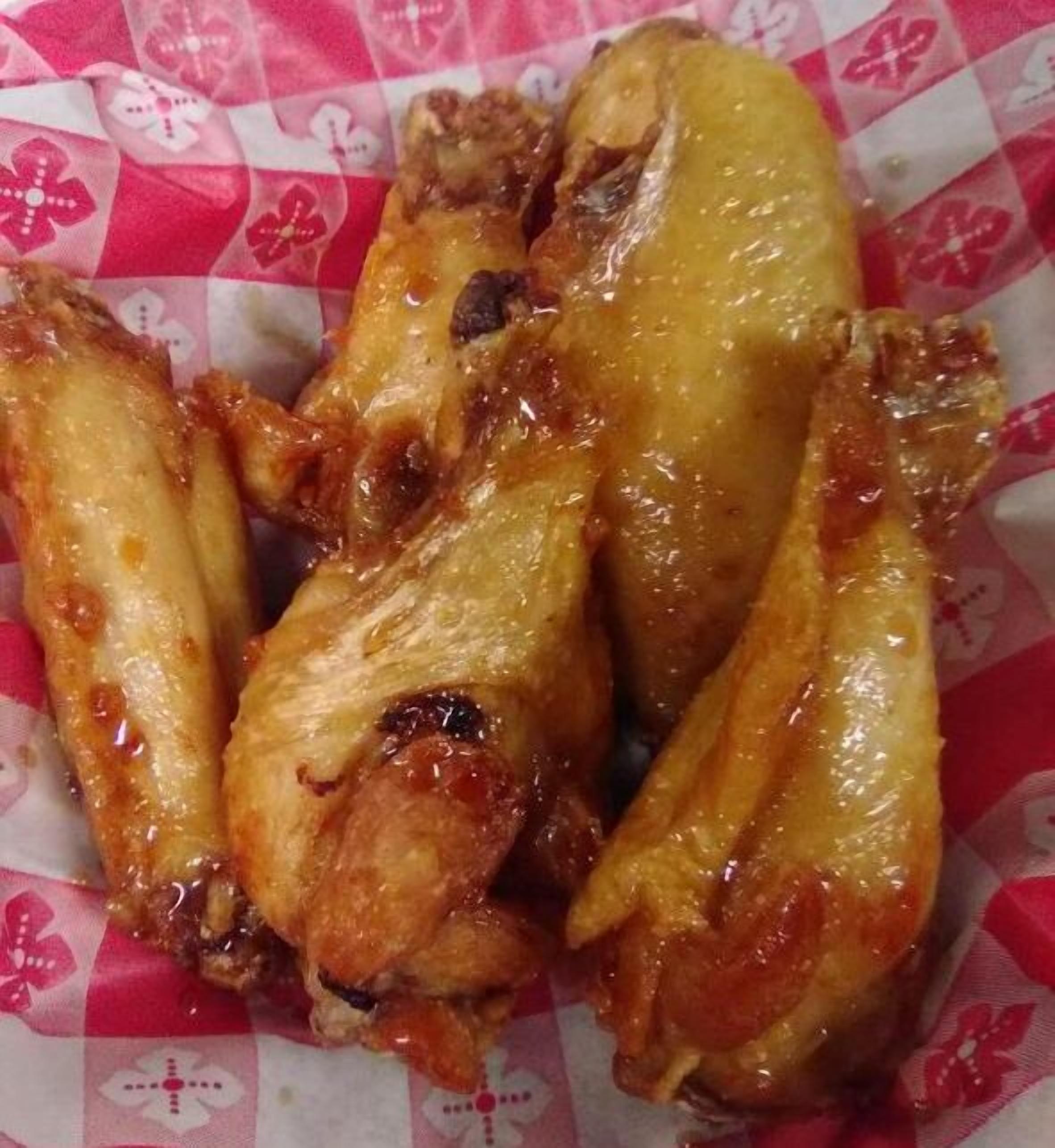 A close-up of chicken wings with a glaze, served on a paper with a floral pattern.