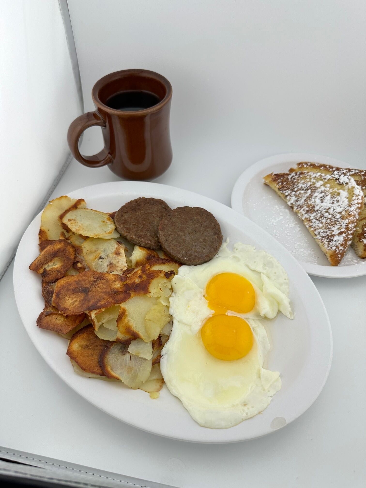Un plato de comida para el desayuno con huevos revueltos, tortitas de patata y salchicha, acompañado de una taza de café y una rebanada de tostada.
