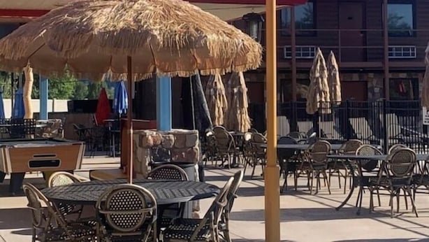 An outdoor seating area with tables and chairs, a thatched umbrella, and a palm tree sculpture. - Beverly hills inn (Aberdeen)