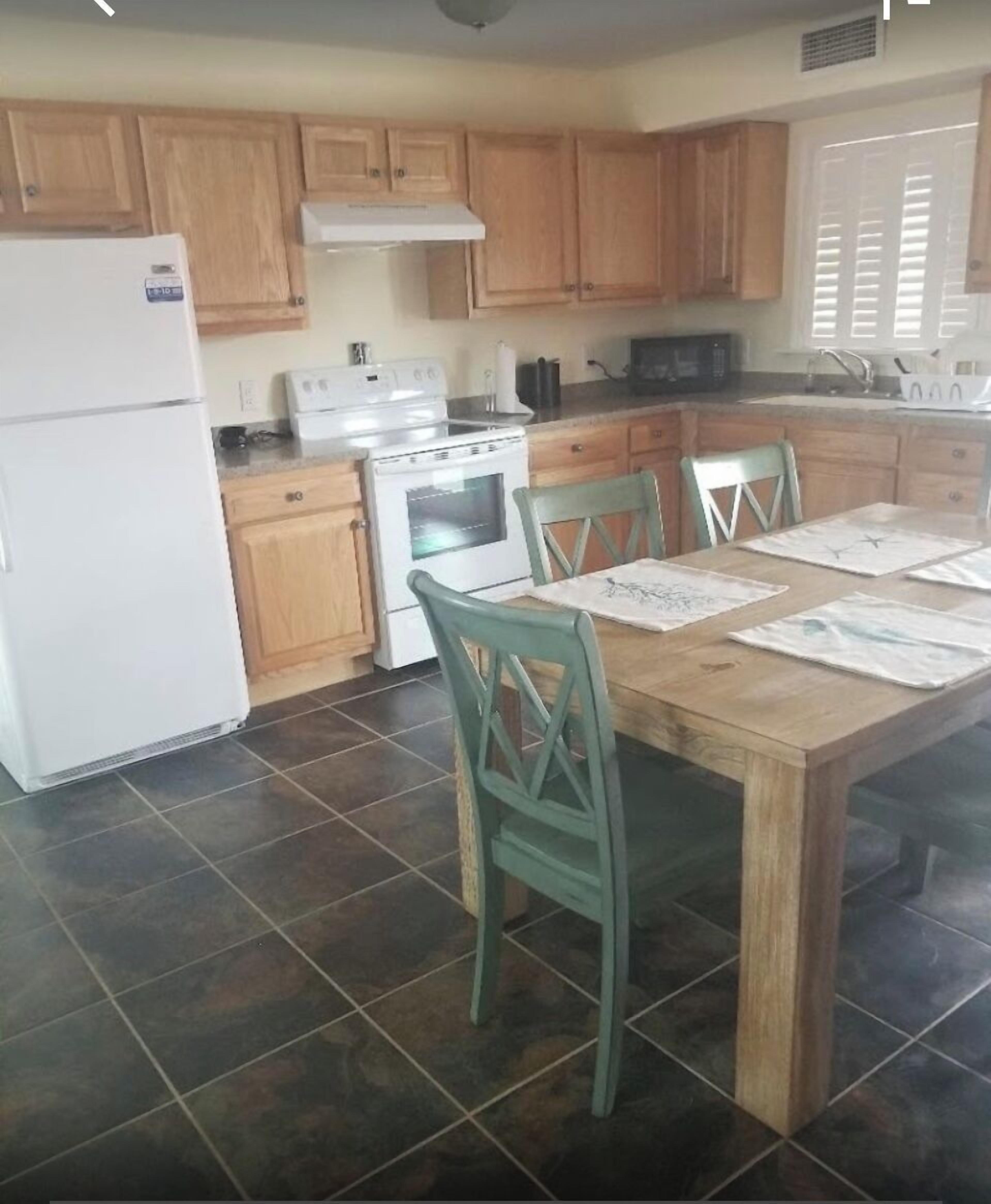 A kitchen with wooden cabinets, a stove, a refrigerator, and a dining table with chairs.