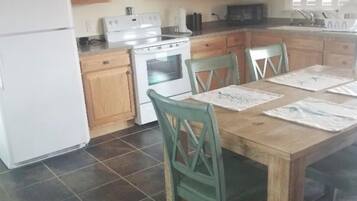 A kitchen with wooden cabinets, a stove, a refrigerator, and a dining table with chairs.