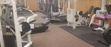 A gym with various exercise equipment, including weight machines and cardio machines, arranged on mats.