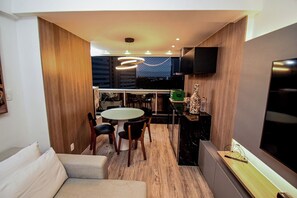Ein modernes Wohnzimmer mit einer Couch, einem Essbereich mit rundem Tisch und Stühlen, einer Küche mit Fernseher und Holzboden.