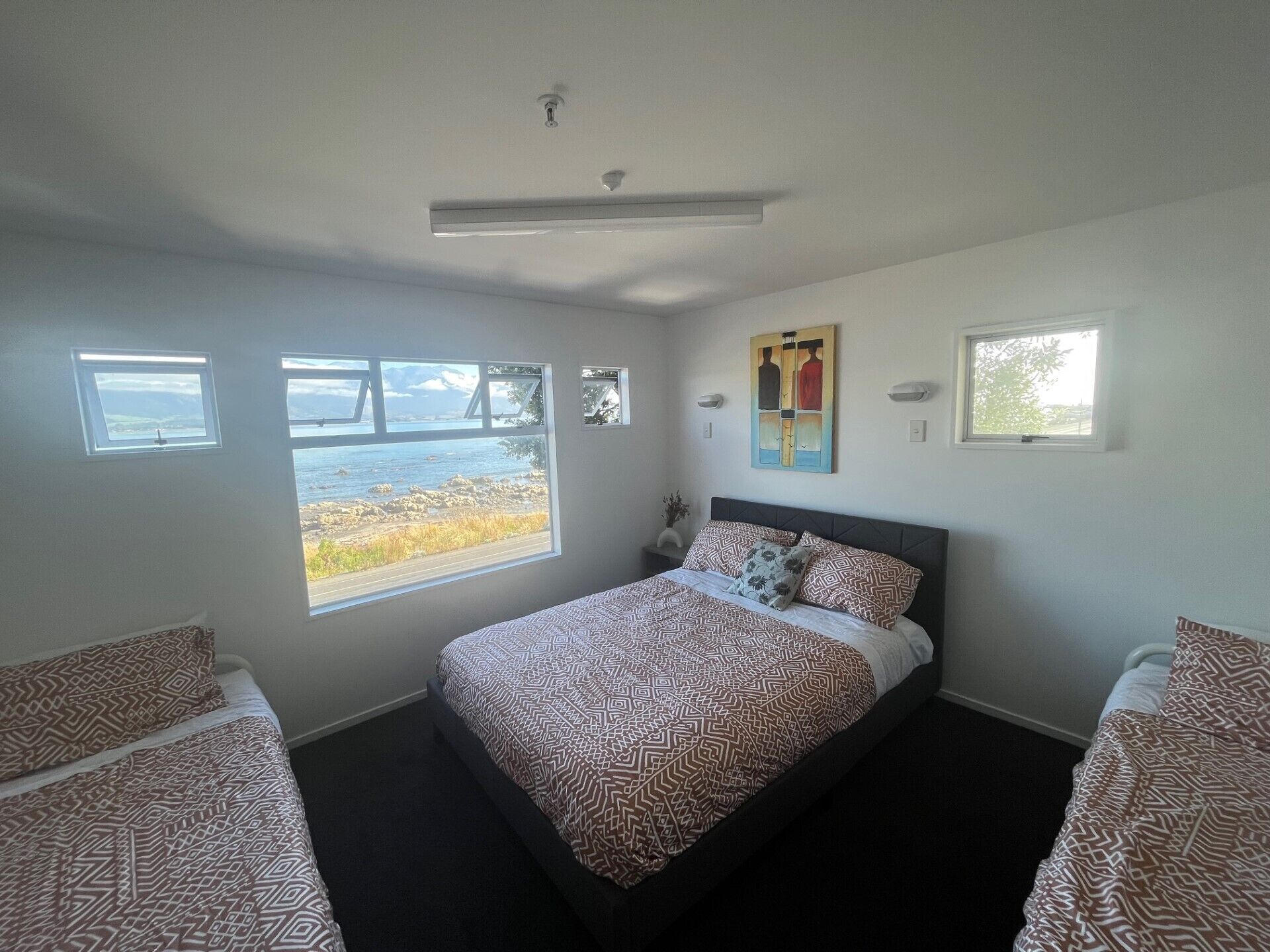 A bedroom with a bed, two bedside tables, a window with a view of the sea, and a ceiling light.