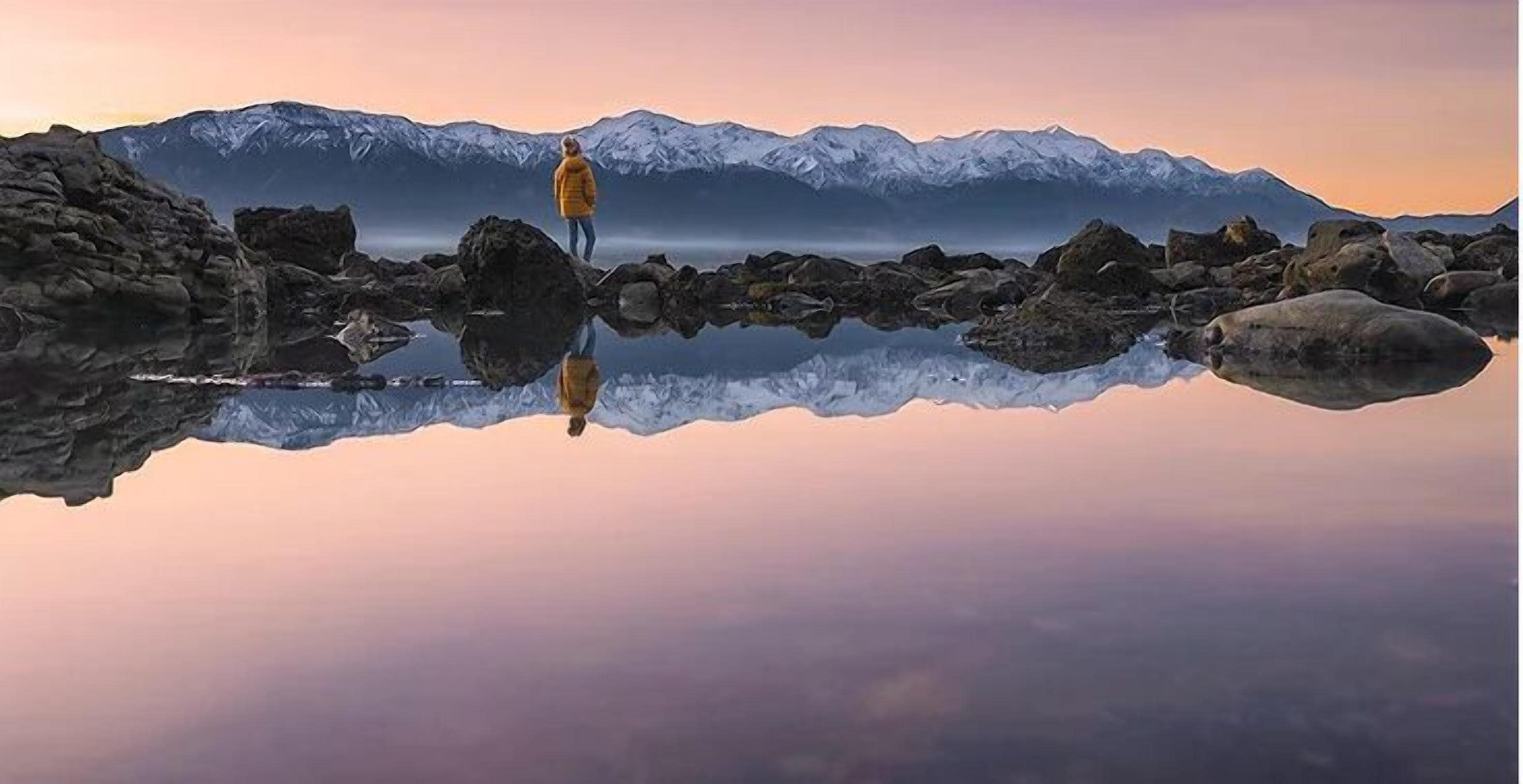 A person standing on a rock formation with a mountain range in the background.