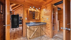 Een houten chalet van binnen, met een keukenhoek, een wastafel en spiegel erboven, en een deur naar een andere kamer.