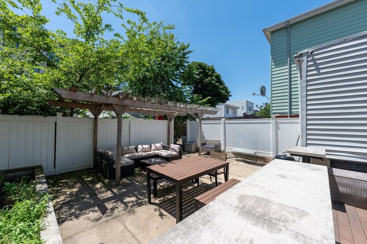 A backyard with a wooden pergola, a sectional sofa, a dining table, and a patio area.