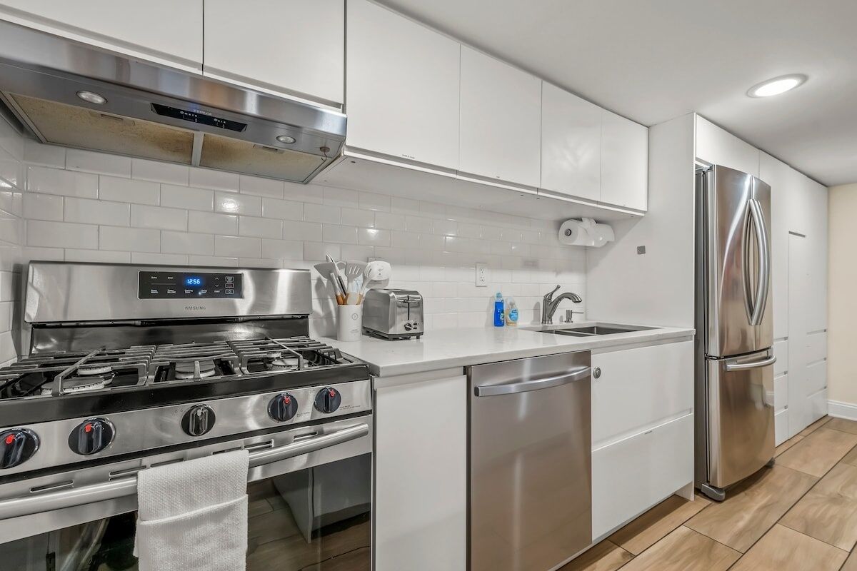 Una cocina moderna con armarios blancos, electrodomésticos de acero inoxidable, una estufa a gas, un lavavajillas y un refrigerador.