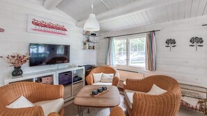 A cozy living room with wicker furniture, a flat-screen TV, and a window with curtains.