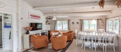 A spacious living area with a television, wicker furniture, and a dining table with chairs.