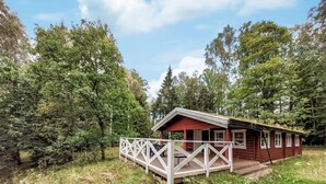 A cabin with a wooden deck and a white railing, surrounded by dense forest.