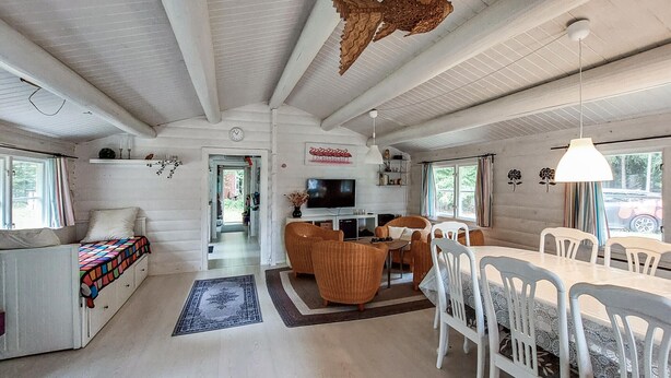 A spacious living area with a sofa, dining table, and chairs, a television, and a large window with curtains.