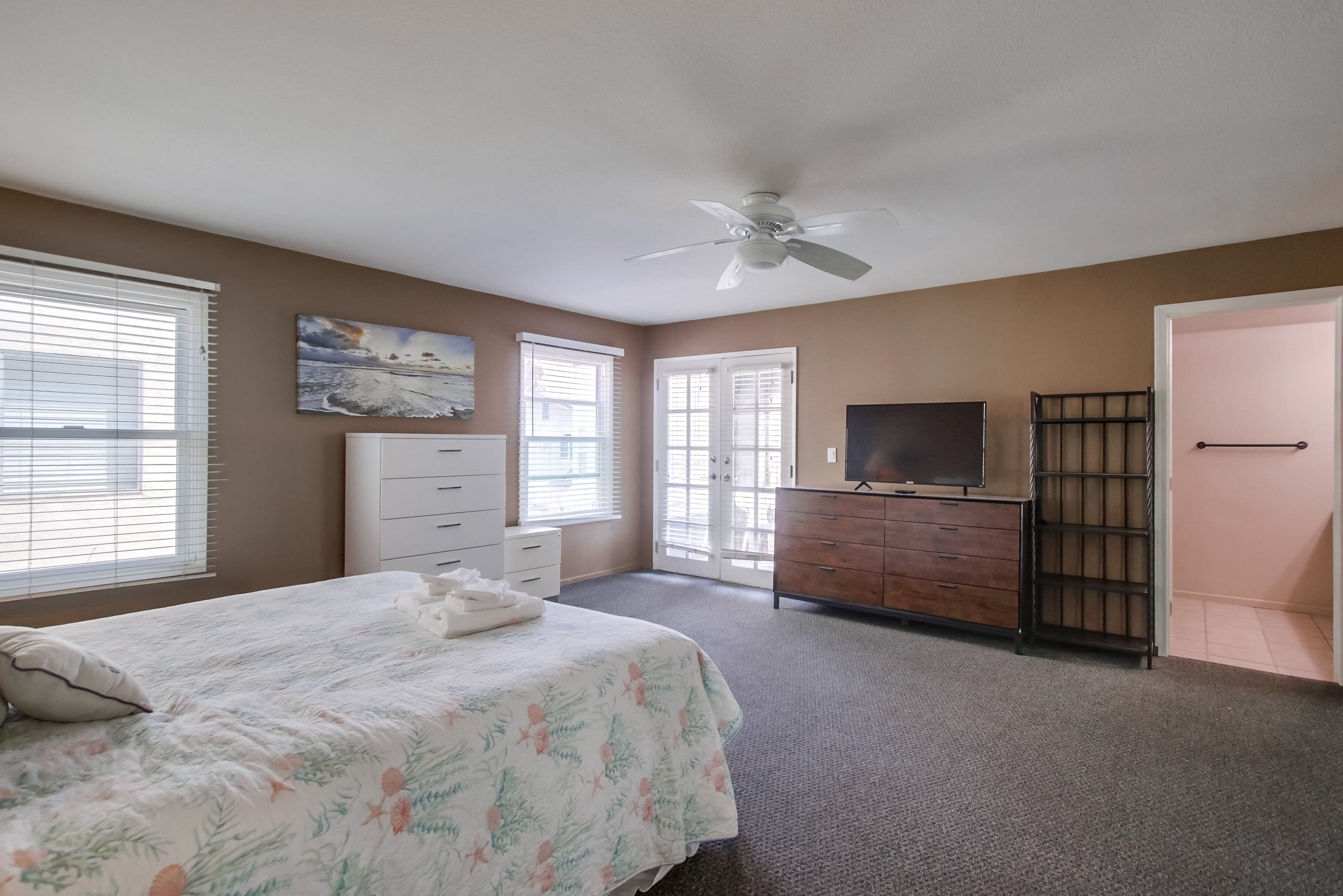 A bedroom with a bed, dresser, television, and a ceiling fan.