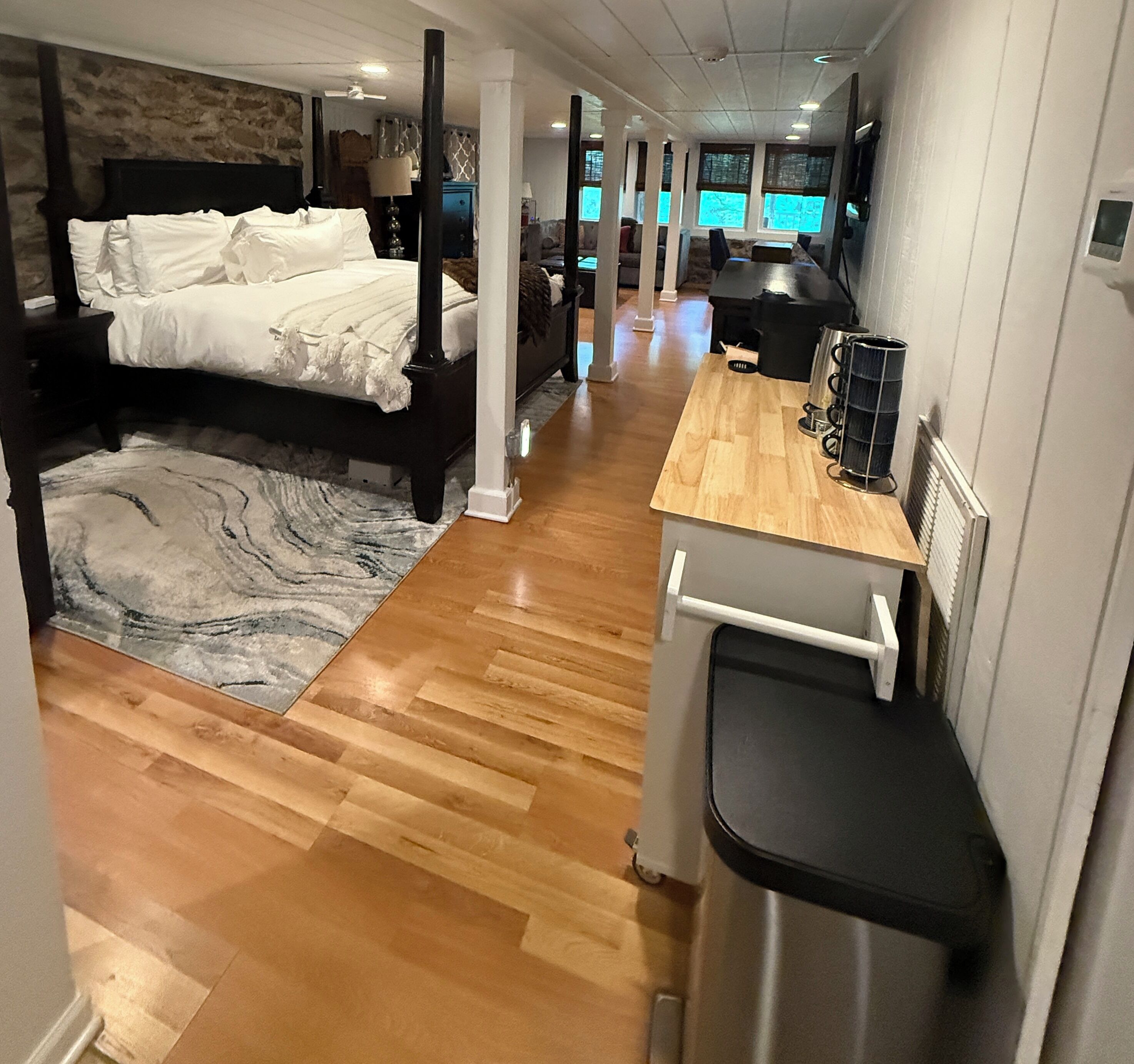 Een moderne hotelkamer met een groot bed, een houten vloer, een kleine kitchenette en uitzicht op de stad door grote ramen.