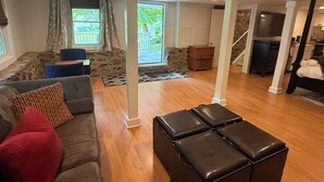 A spacious living room with a grey sofa, a black ottoman, and a stone fireplace.
