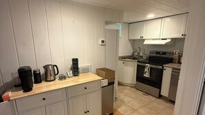A kitchen with white cabinets, a wooden countertop, a coffee maker, and a stove.