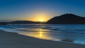 A beach scene with a sunset, calm waves, and a distant mountain. - Charming Cottage by the Water Pet Friendly WoyWoy (Woy Woy)