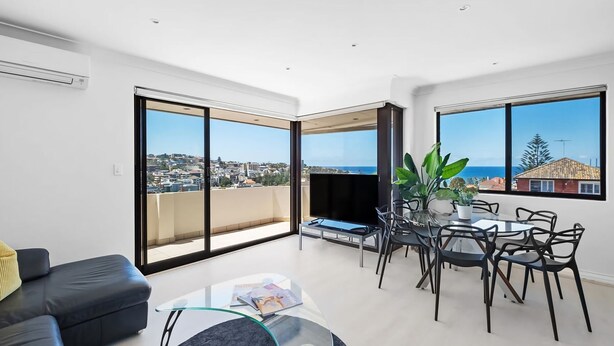 A spacious living area with a balcony, a dining set, and a sofa. - Dream View Steps from the Beach (Coogee)