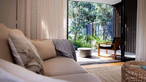 Un salon moderne avec un canapé, un fauteuil et une vue sur un jardin grâce à de grandes fenêtres.