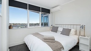 A modern bedroom with a large bed, a view of a cityscape, and a window with blinds.