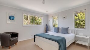A bedroom with a large bed, two windows, a chair, and a nightstand. - Oceanview Escape One Hour from Sydney (Wombarra)